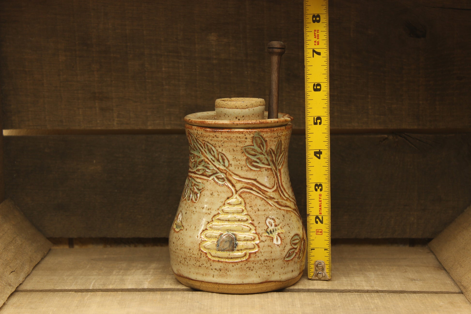 Ceramic honey pot with beehive and bees with a wood honey dipper with measuring tape