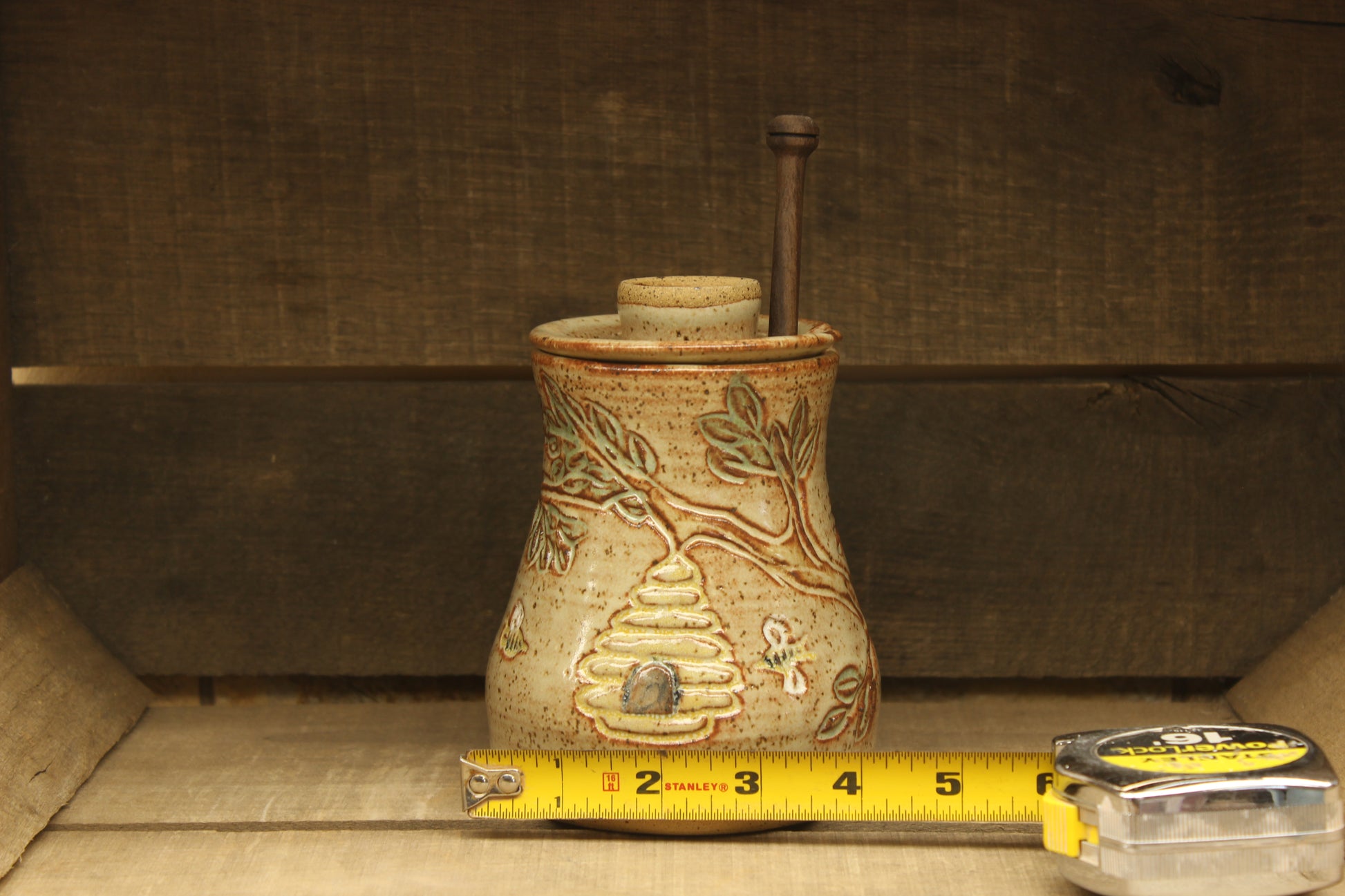Ceramic honey pot with beehive and bees with a wood honey dipper with measuring tape