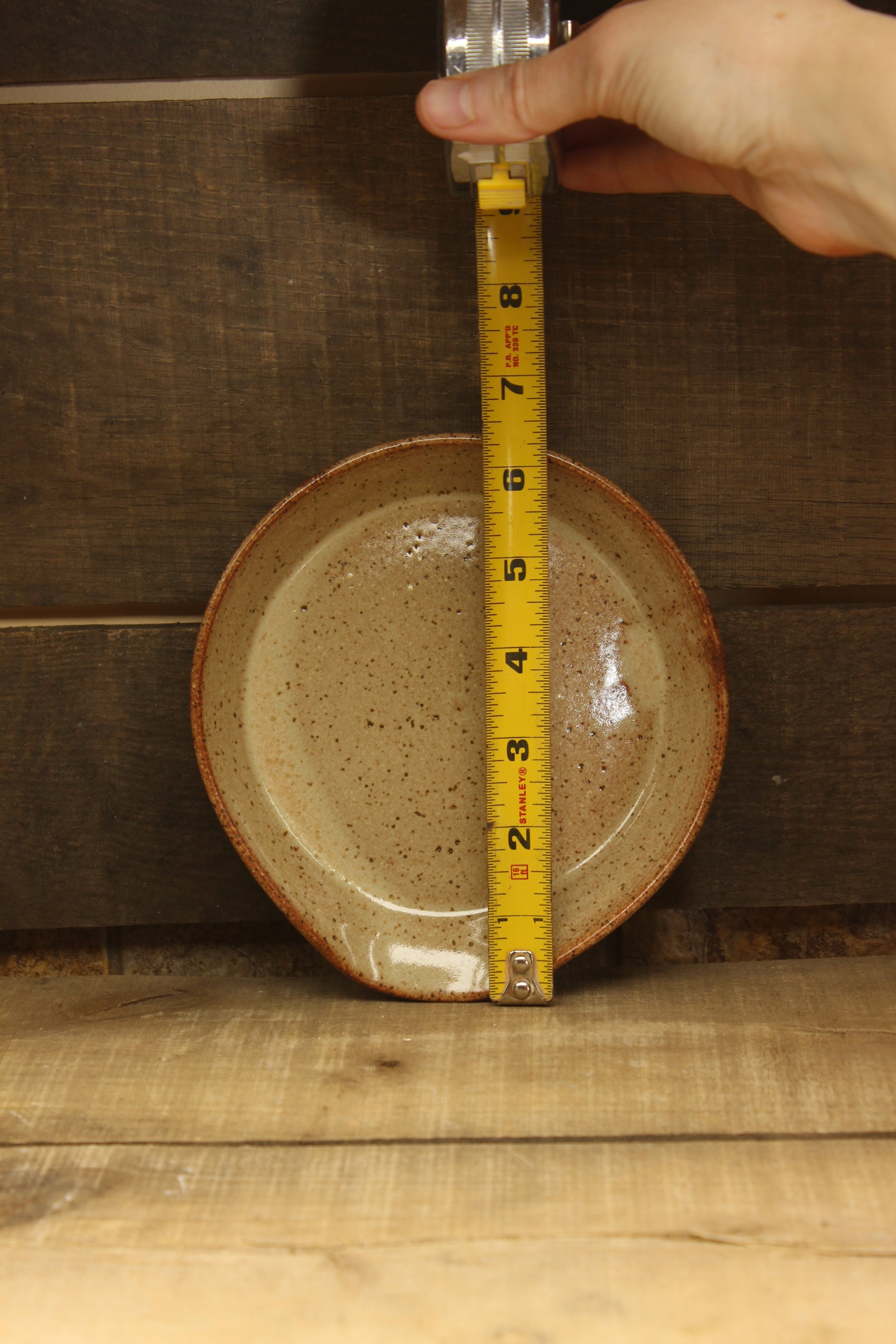 Ceramic plate being measured with a tape measure on a wooden surface