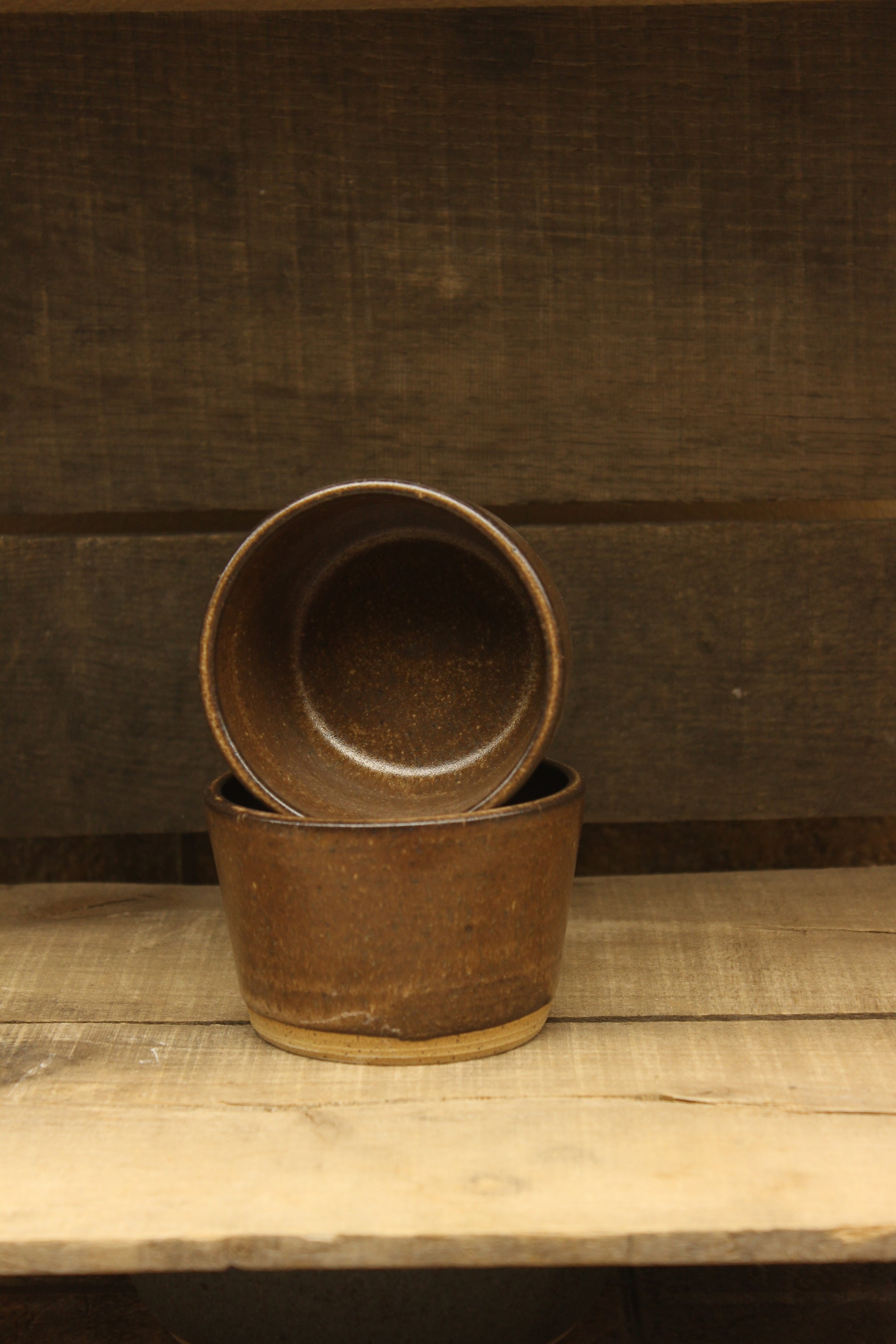 2 Brown ceramic cups on a wooden surface