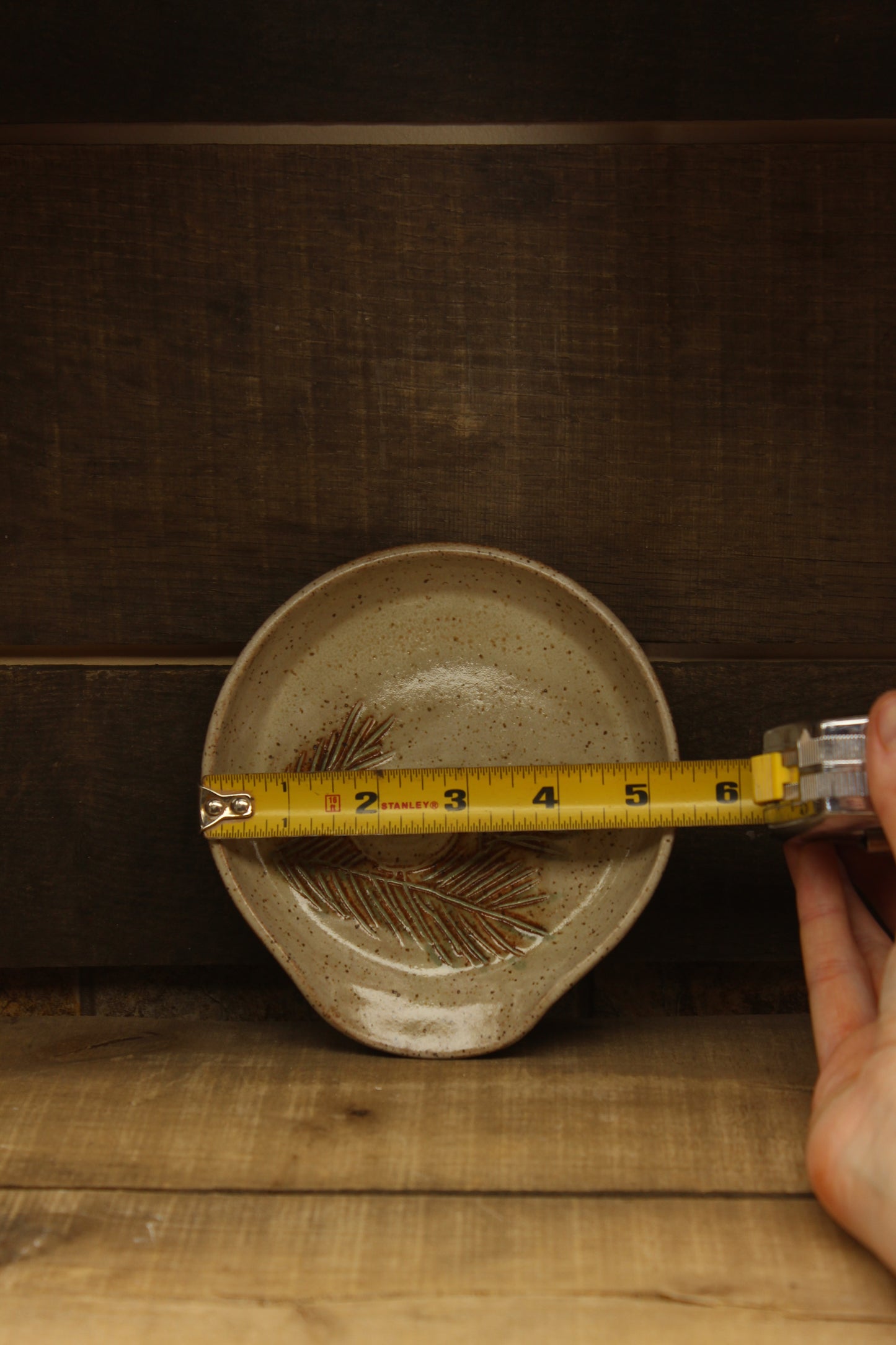 Ceramic dish with chickadee and pine branch design on a wooden surface with tape measure
