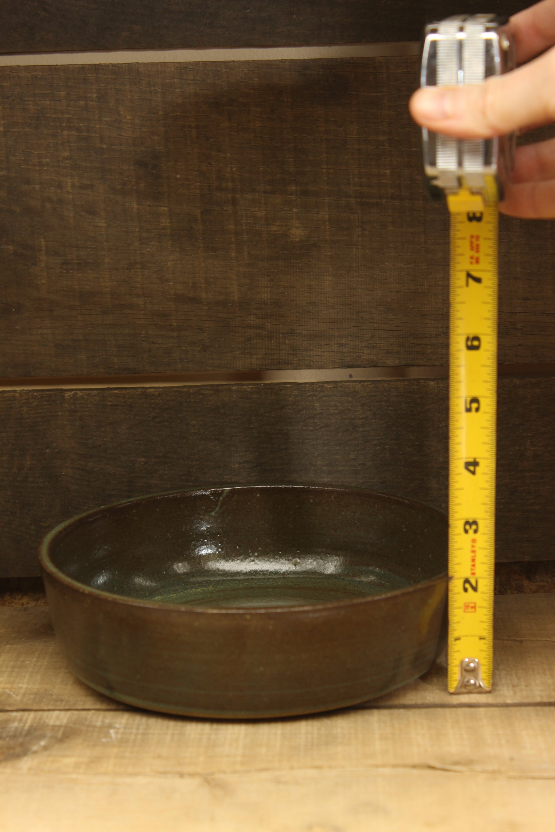 Measuring a green shallow bowl with a tape measure on a wooden surface