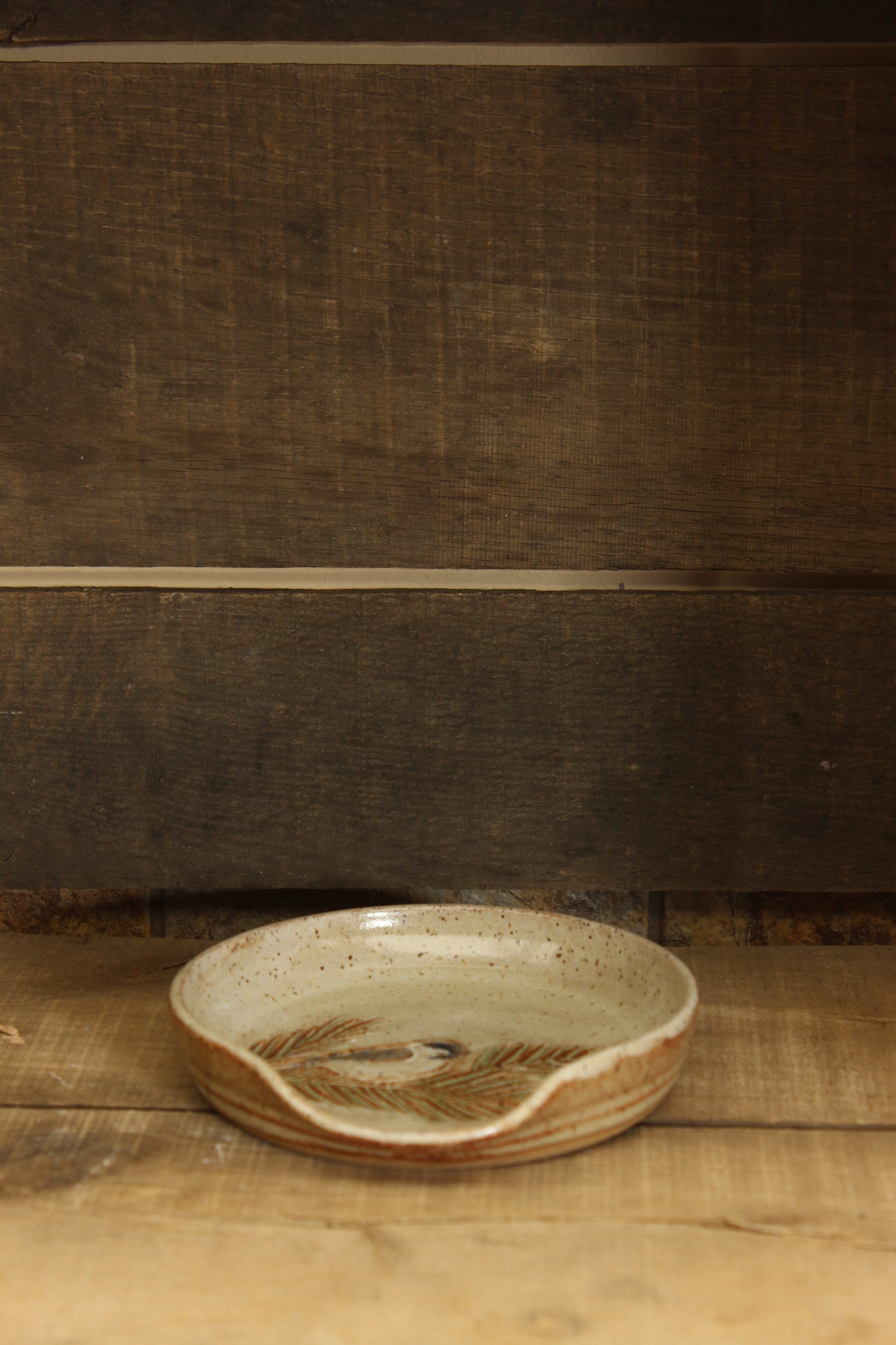 Ceramic dish with chickadee and pine branch design on a wooden surface with tape measure