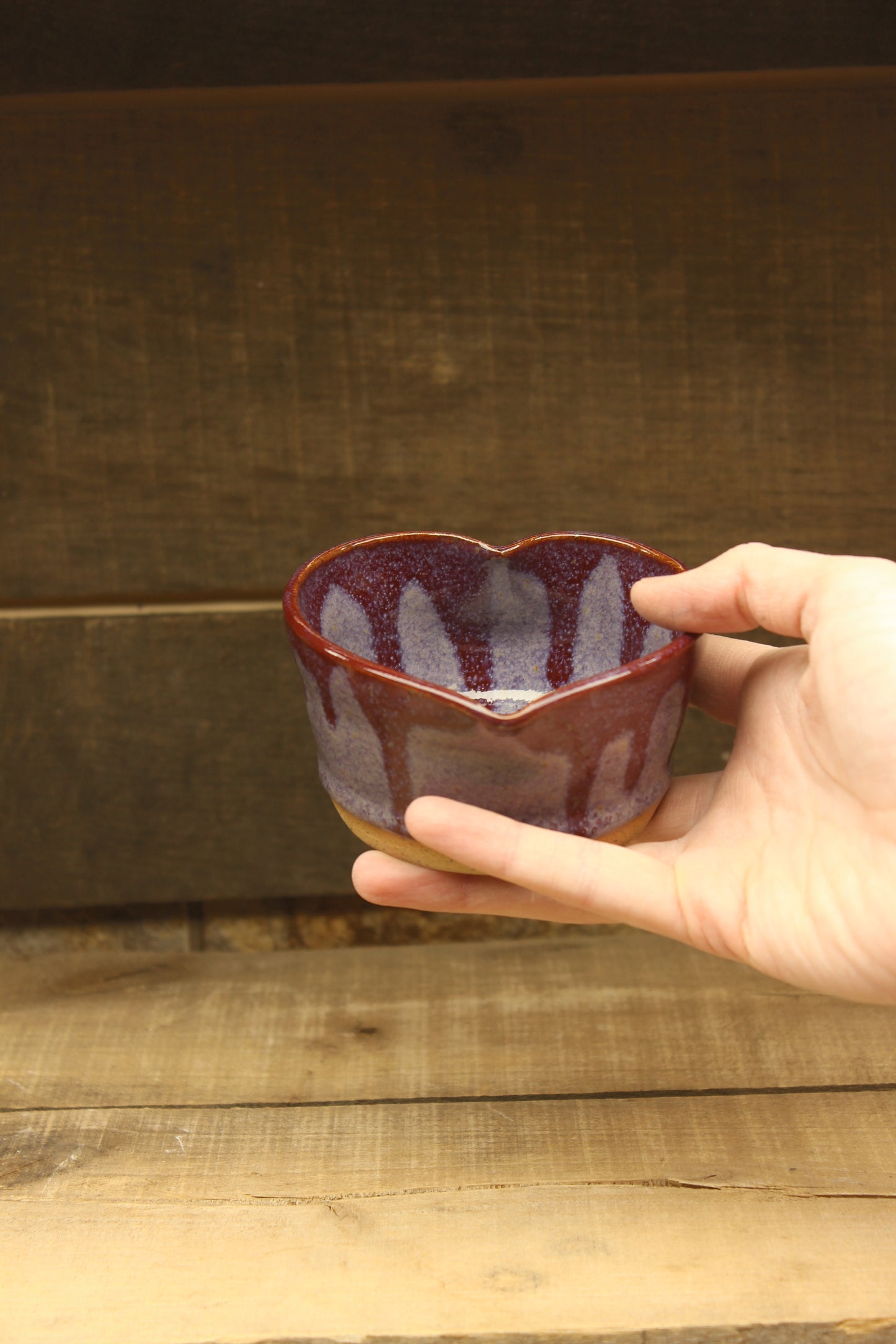 Heart-shaped purple bowl held by a hand against a wooden background