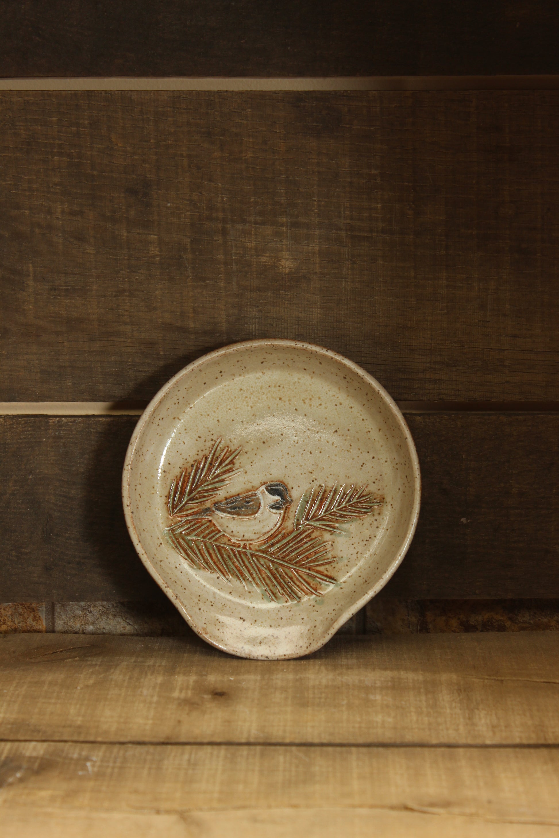 Ceramic dish with chickadee and pine branch design on a wooden surface